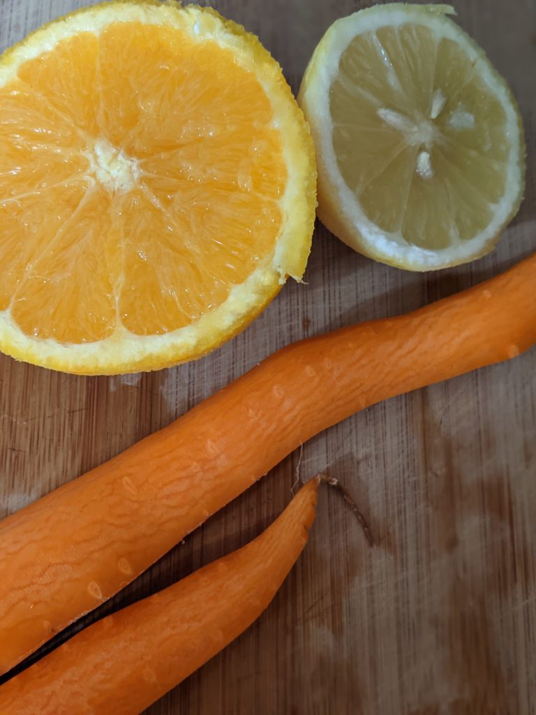 A sliced orange, a sliced lemon, and peeled carrots rest on a cutting board.